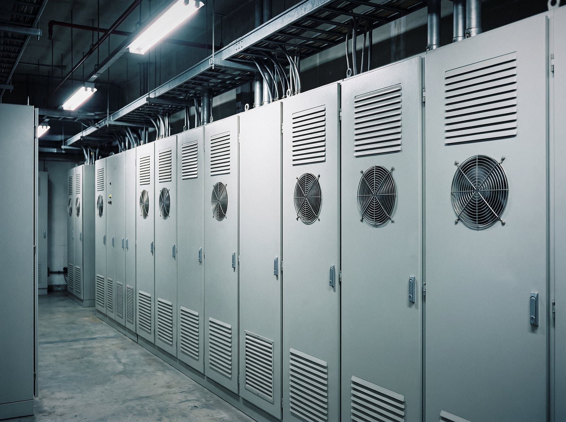 Illustrative image: row of fan-cooled electrical enclosures with ventilation louvers in an electrical room